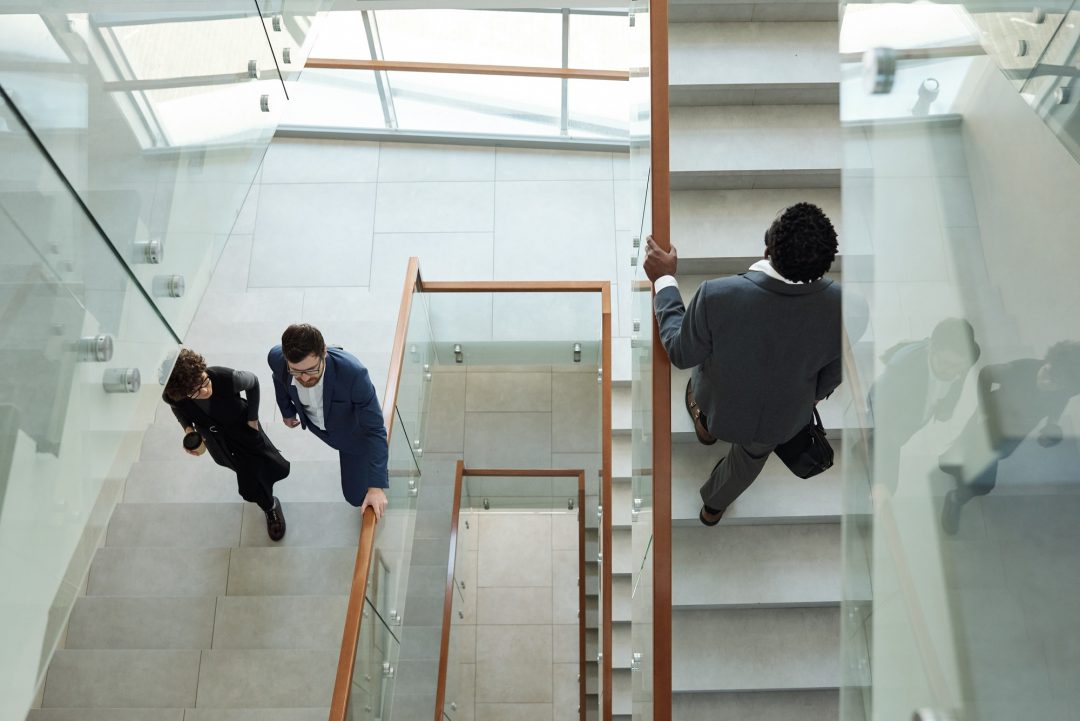 Overview of young intercultural office workers in formalwear going upstairs